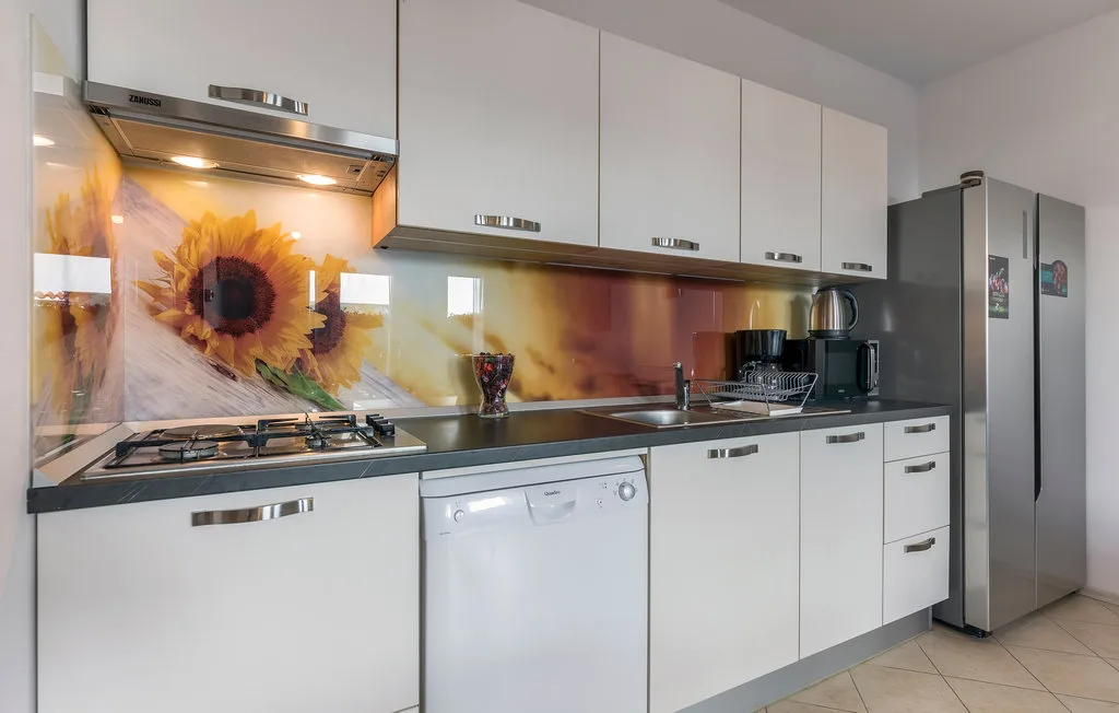 Una cocina moderna con gabinetes blancos, una encimera oscura y un salpicadero con girasol.