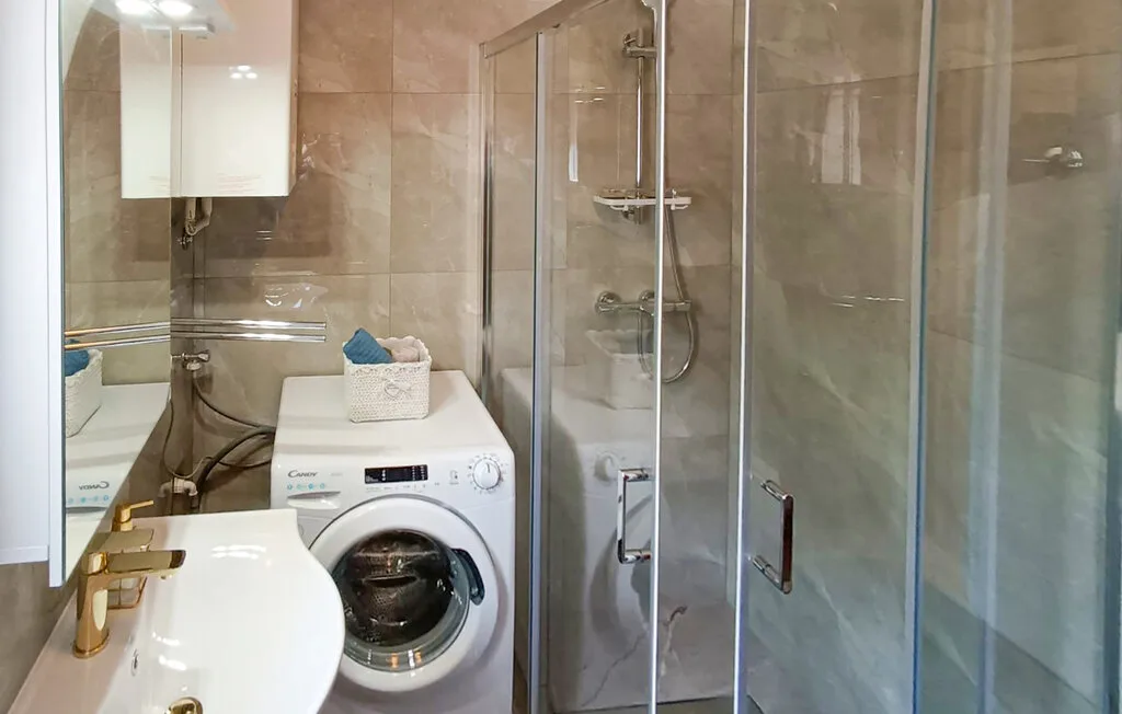 Un baño con lavabo, lavadora y ducha de vidrio.
