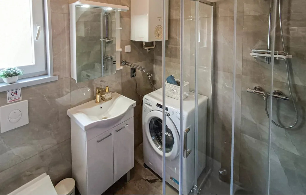 Un baño alicatado con lavabo, lavadora y ducha de vidrio.