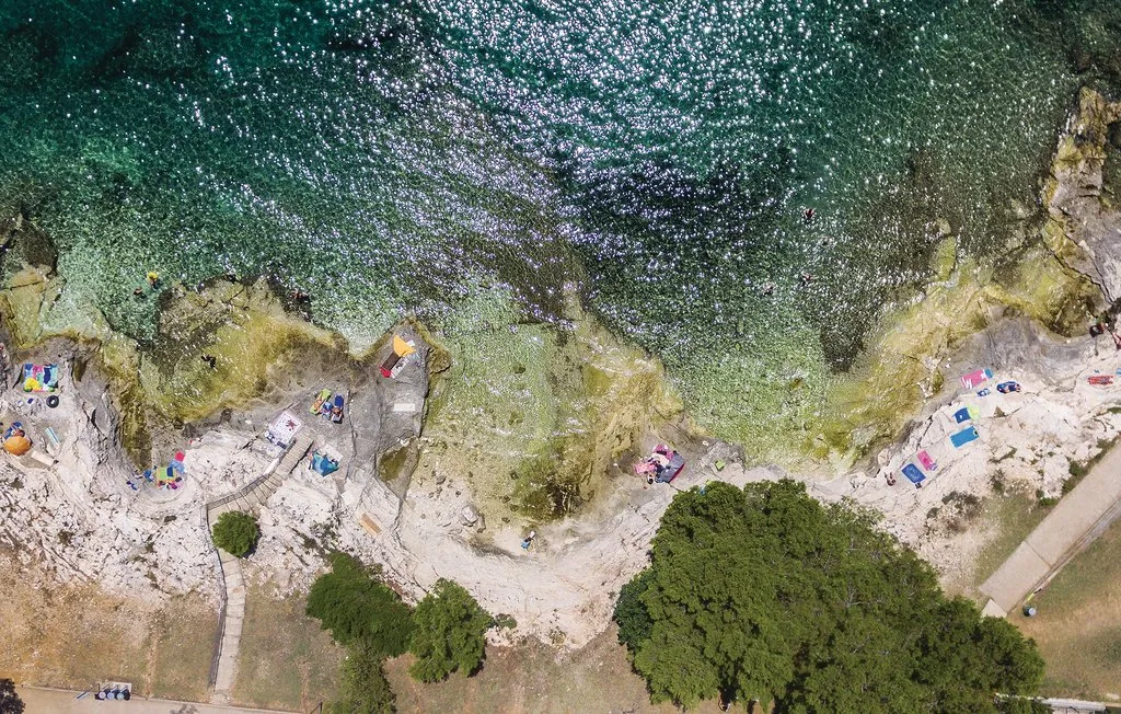 Vista aérea de una costa rocosa con agua clara y bañistas.