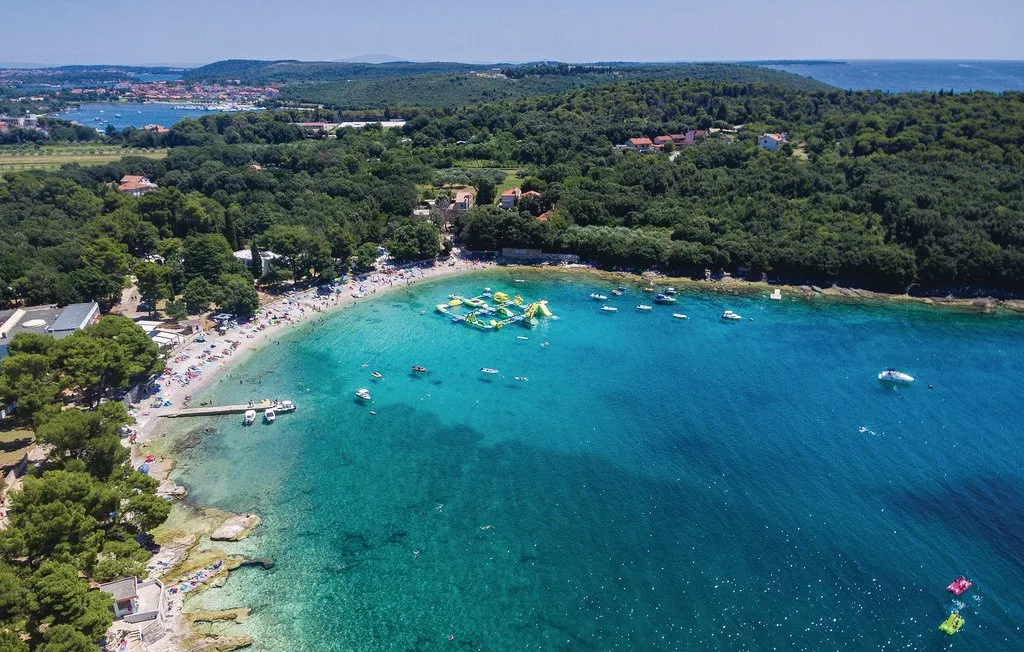 Vista aérea de una playa curva y una bahía turquesa bordeada de colinas verdes.