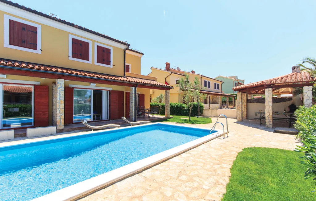 Una piscina junto a un patio pavimentado y una zona de estar cubierta.
