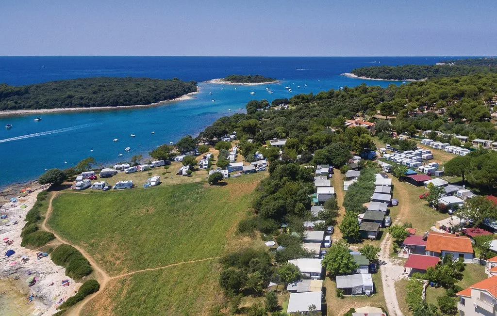 Vista aérea de un camping costero junto a una bahía turquesa y una costa boscosa.