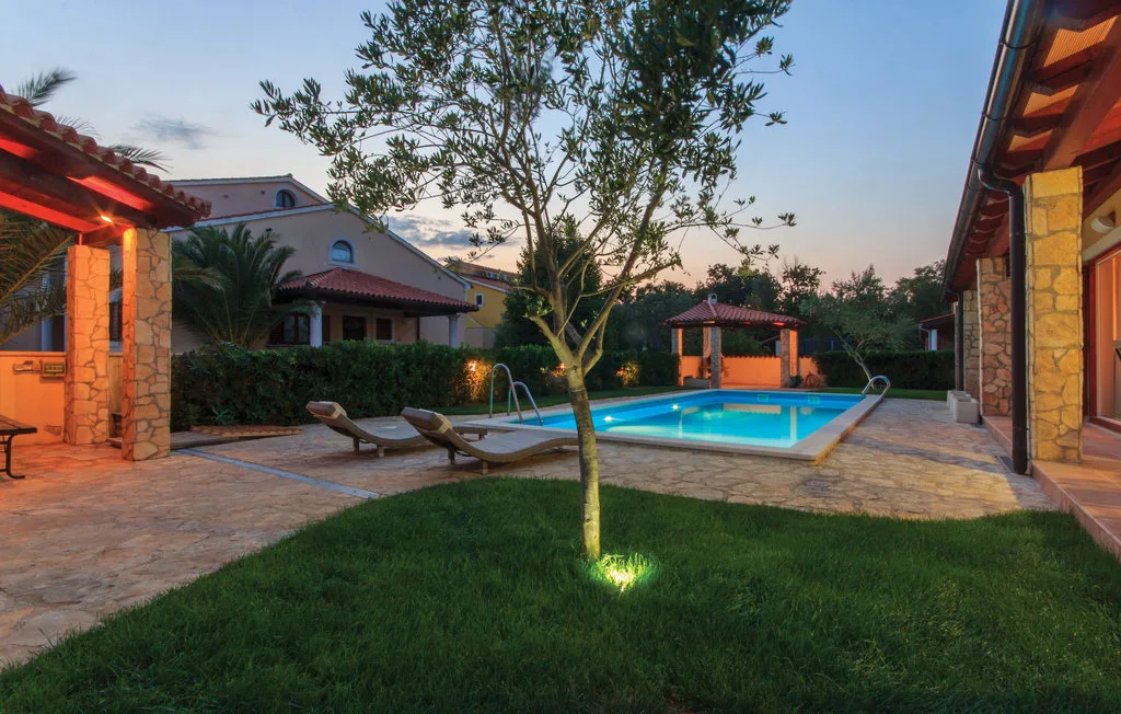 Una zona de piscina al aire libre con asientos, un árbol y pavimento al atardecer.