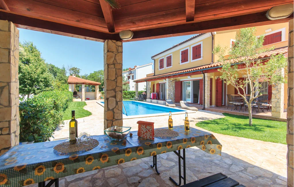 Una zona de comedor al aire libre cubierta da a una piscina y un jardín.