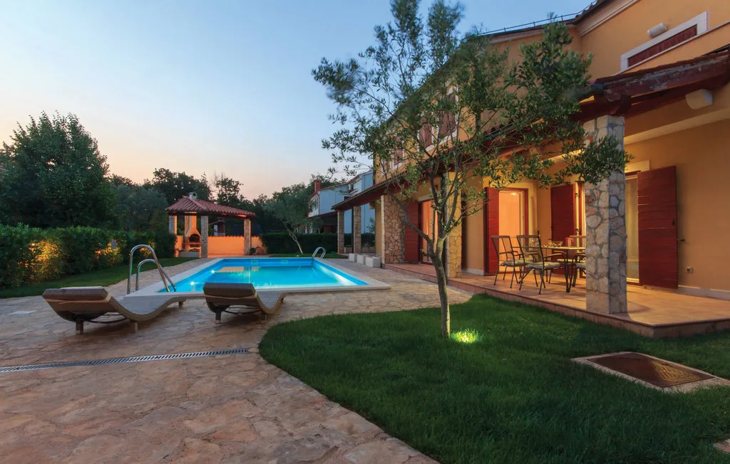 Una piscina al aire libre junto a un patio pavimentado y una casa iluminada.