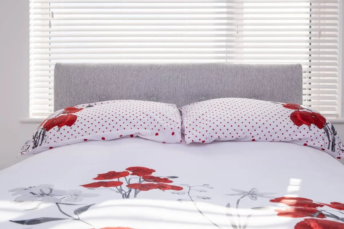 A bed with red floral bedding sits in front of a window with blinds.