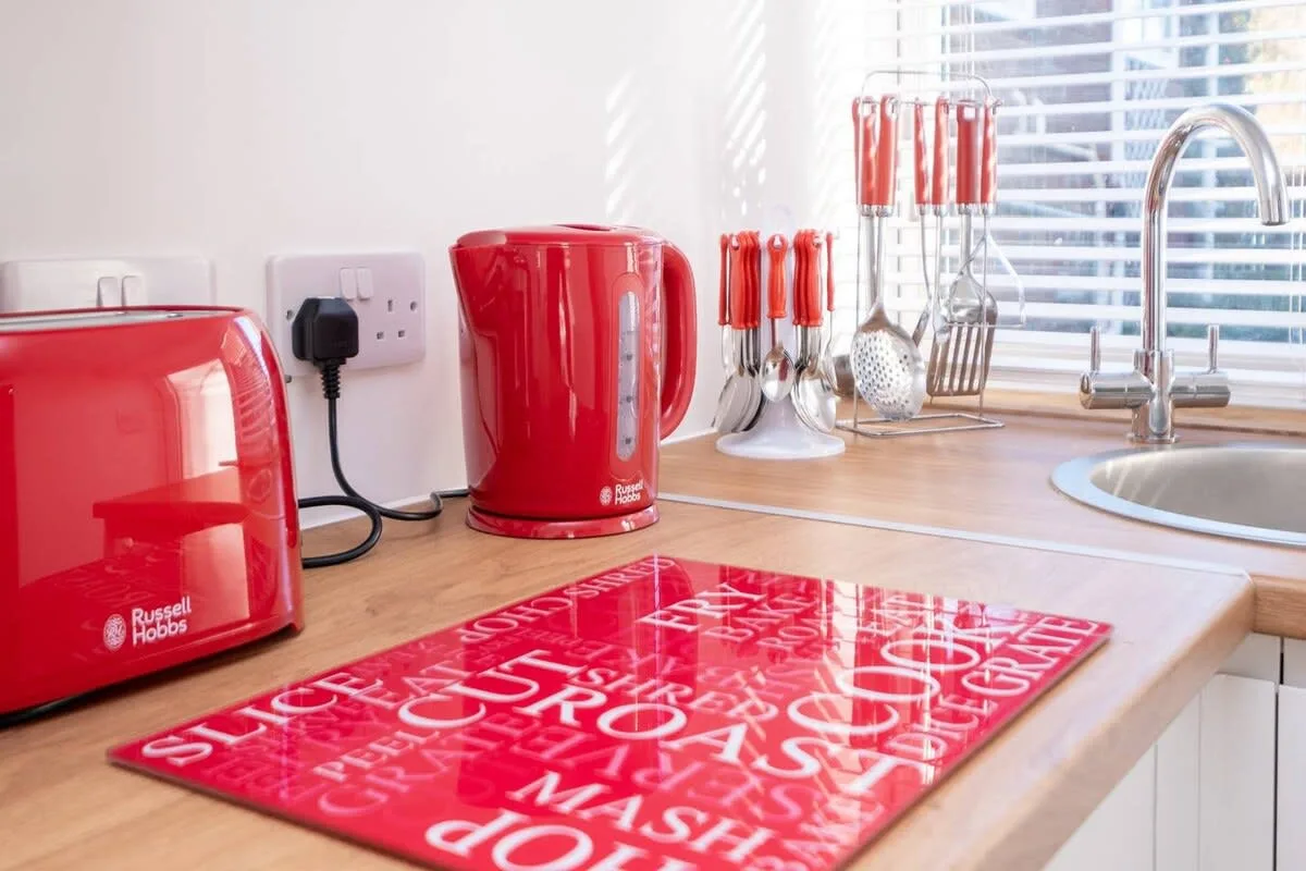 Una encimera de cocina luminosa con electrodomésticos rojos y utensilios junto a una ventana.