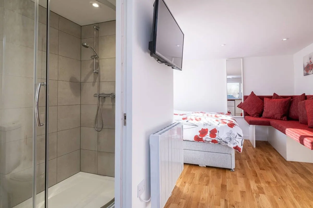 Un estudio con una cama, asientos rojos y una ducha de vidrio.