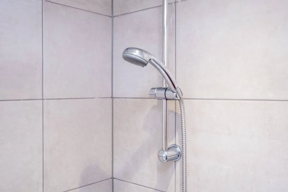 Una pared de ducha alicatada con ducha de mano y manguera.