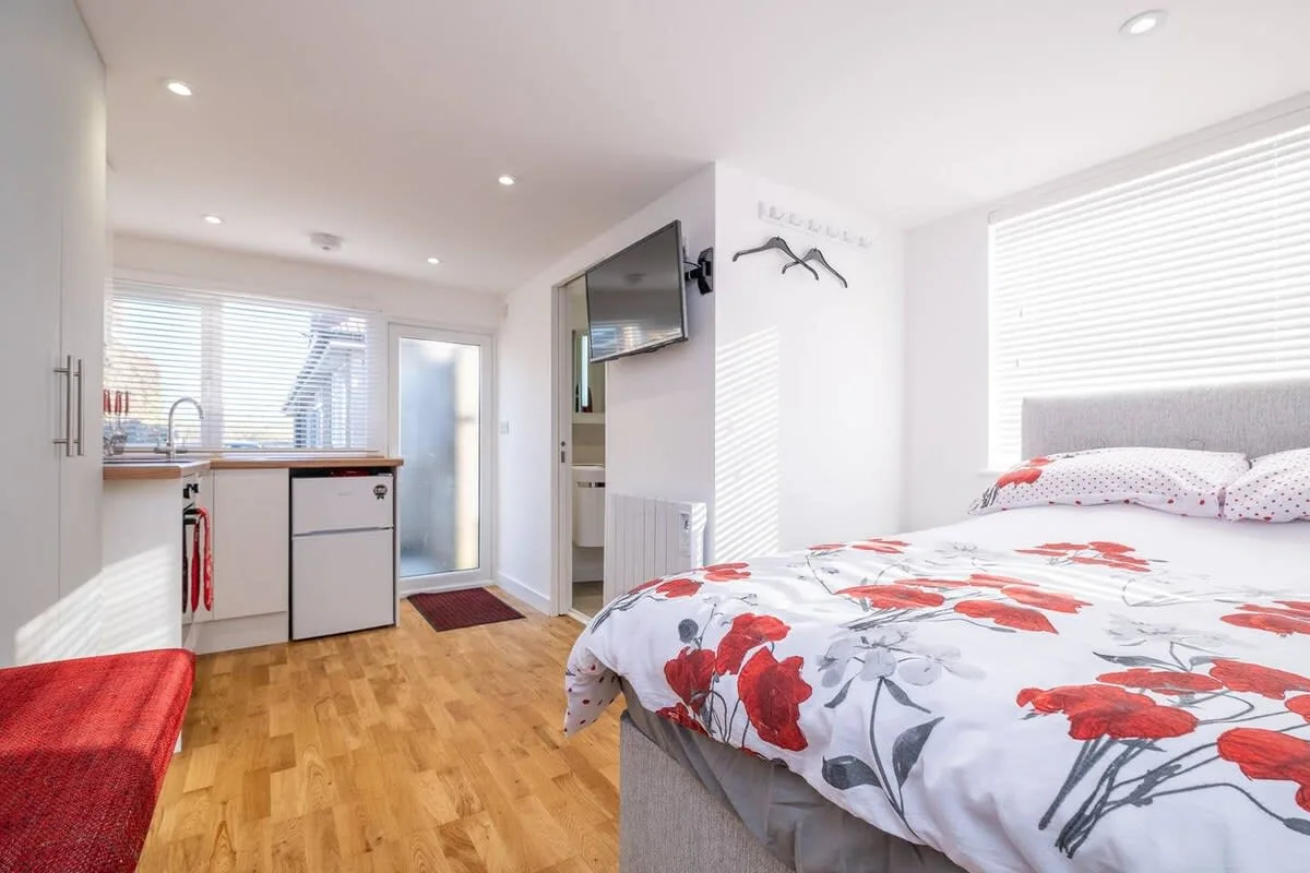 A bright bedroom with a floral bedspread and a compact kitchenette.