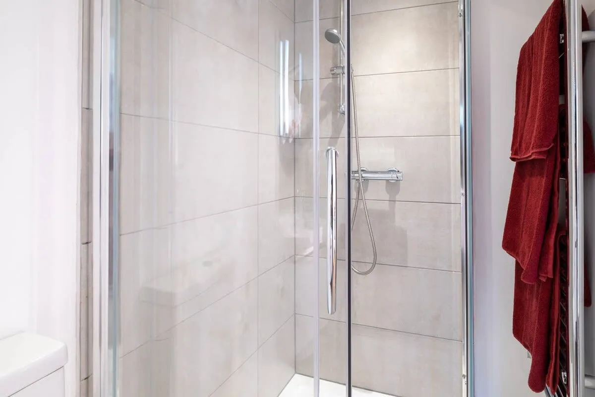 A tiled bathroom shower with a handheld showerhead and red towels.