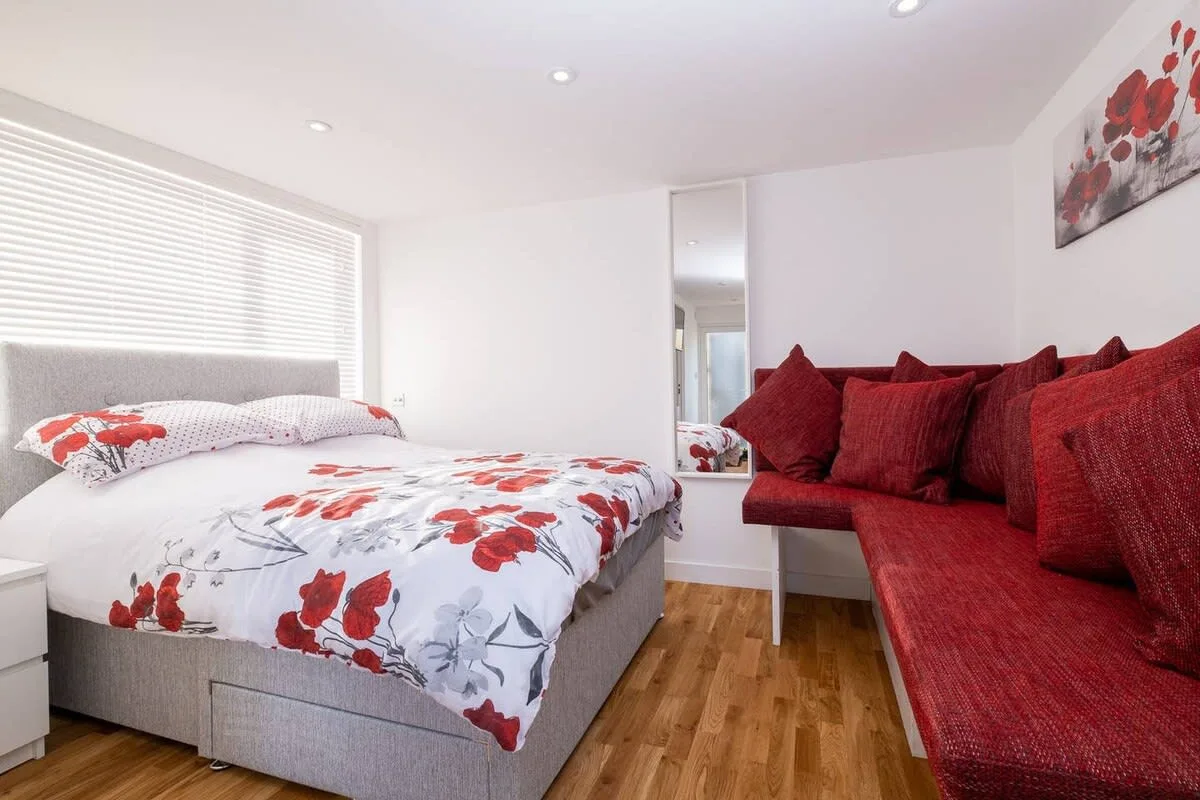 Un dormitorio con una cama cubierta de ropa de cama floral roja junto a asientos rojos.