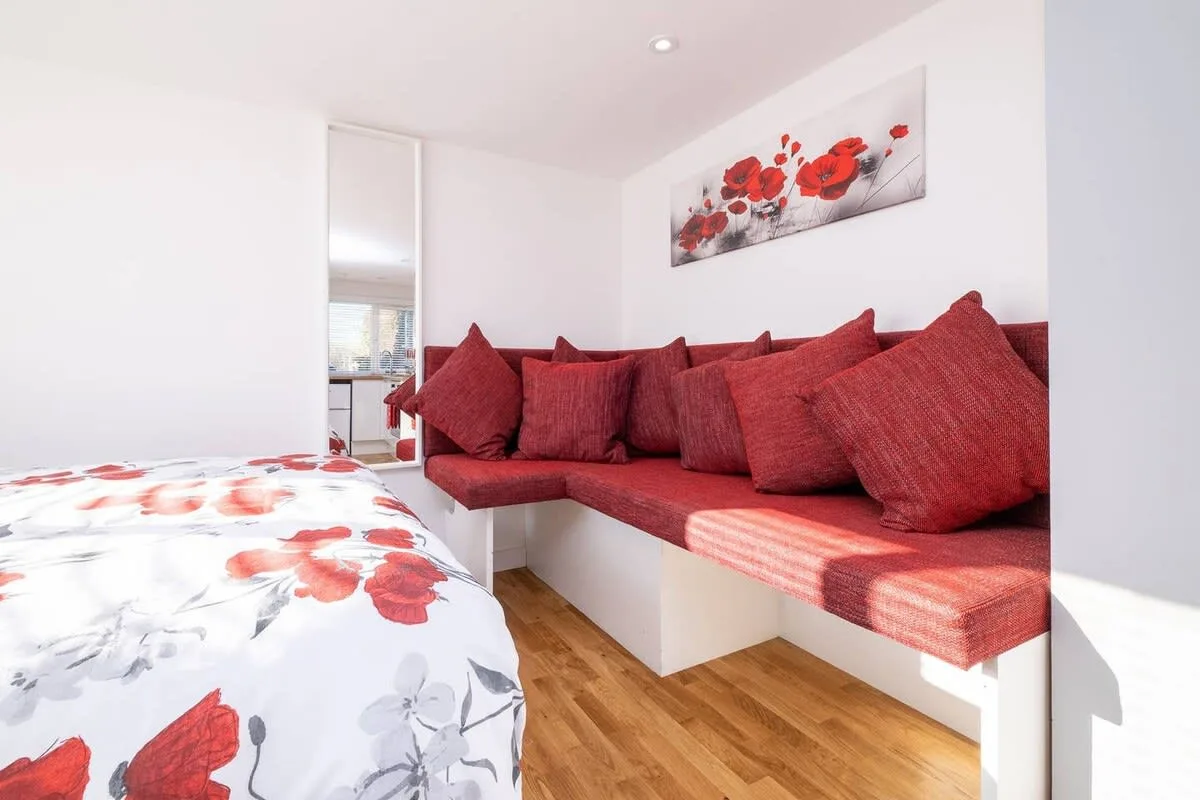 A bright bedroom with a red built-in seating area and floral bedding.