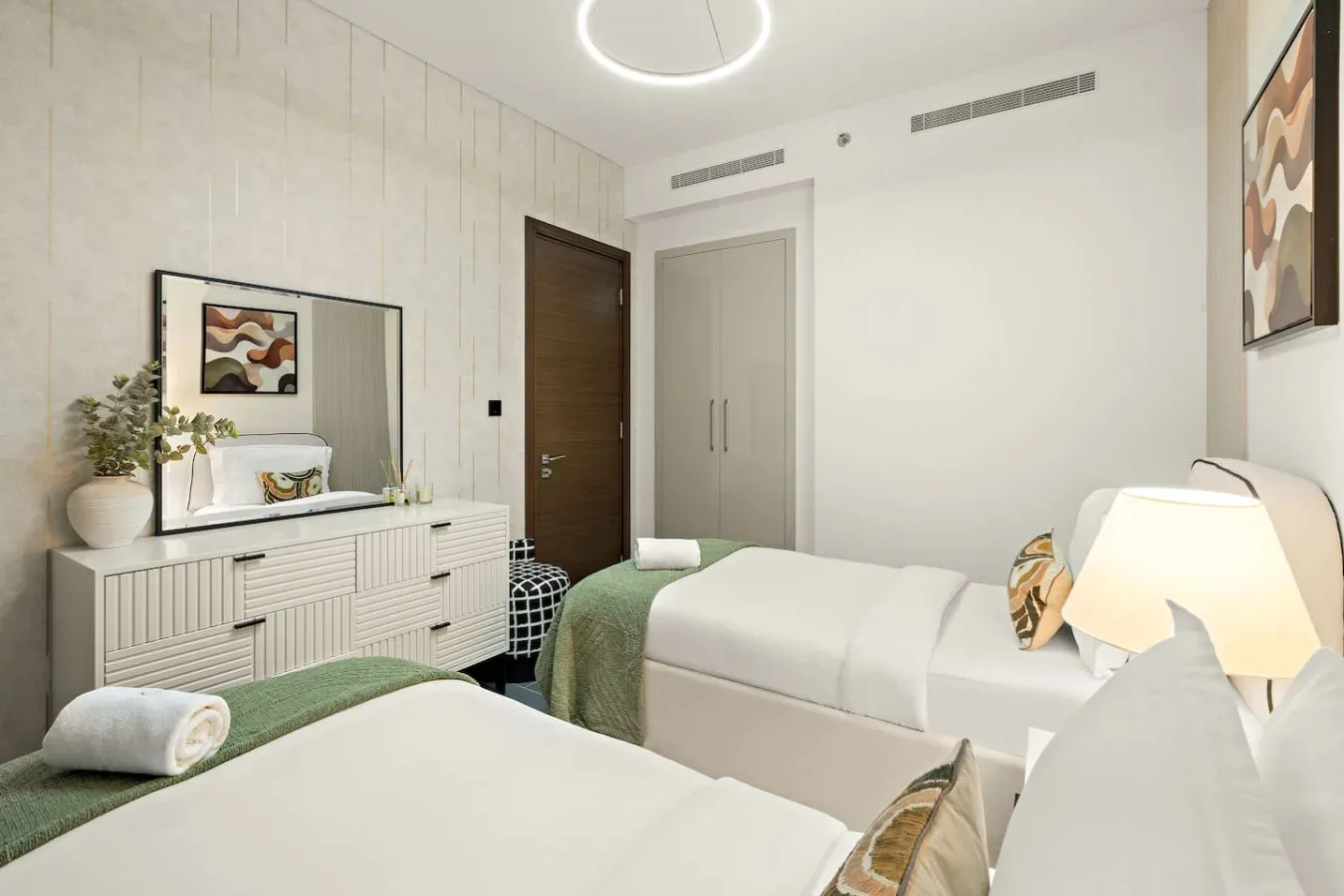 A bright bedroom with two beds, a dresser, and framed wall art.