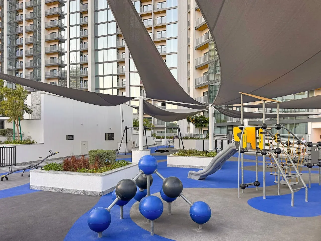 An outdoor playground with blue play equipment and a climbing structure beneath shade canopies.