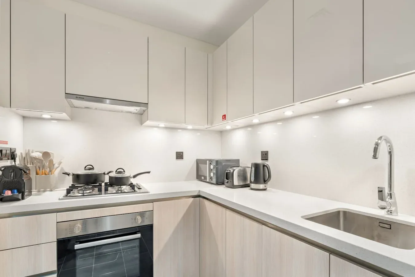 A bright modern kitchen with white cabinets, a cooktop, and a sink.