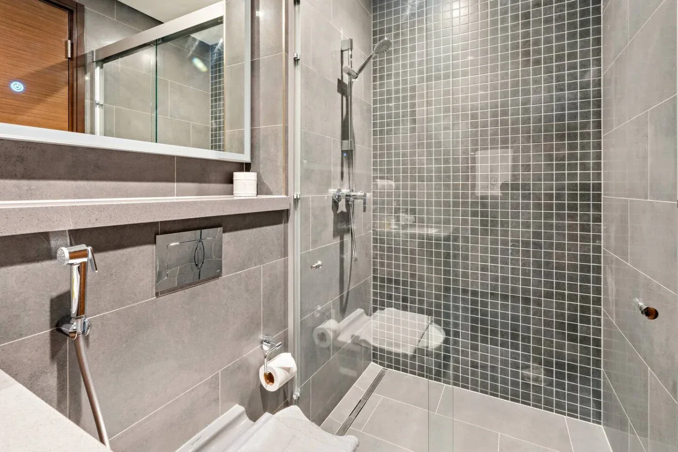 A tiled bathroom with a glass shower and wall-mounted fixtures.