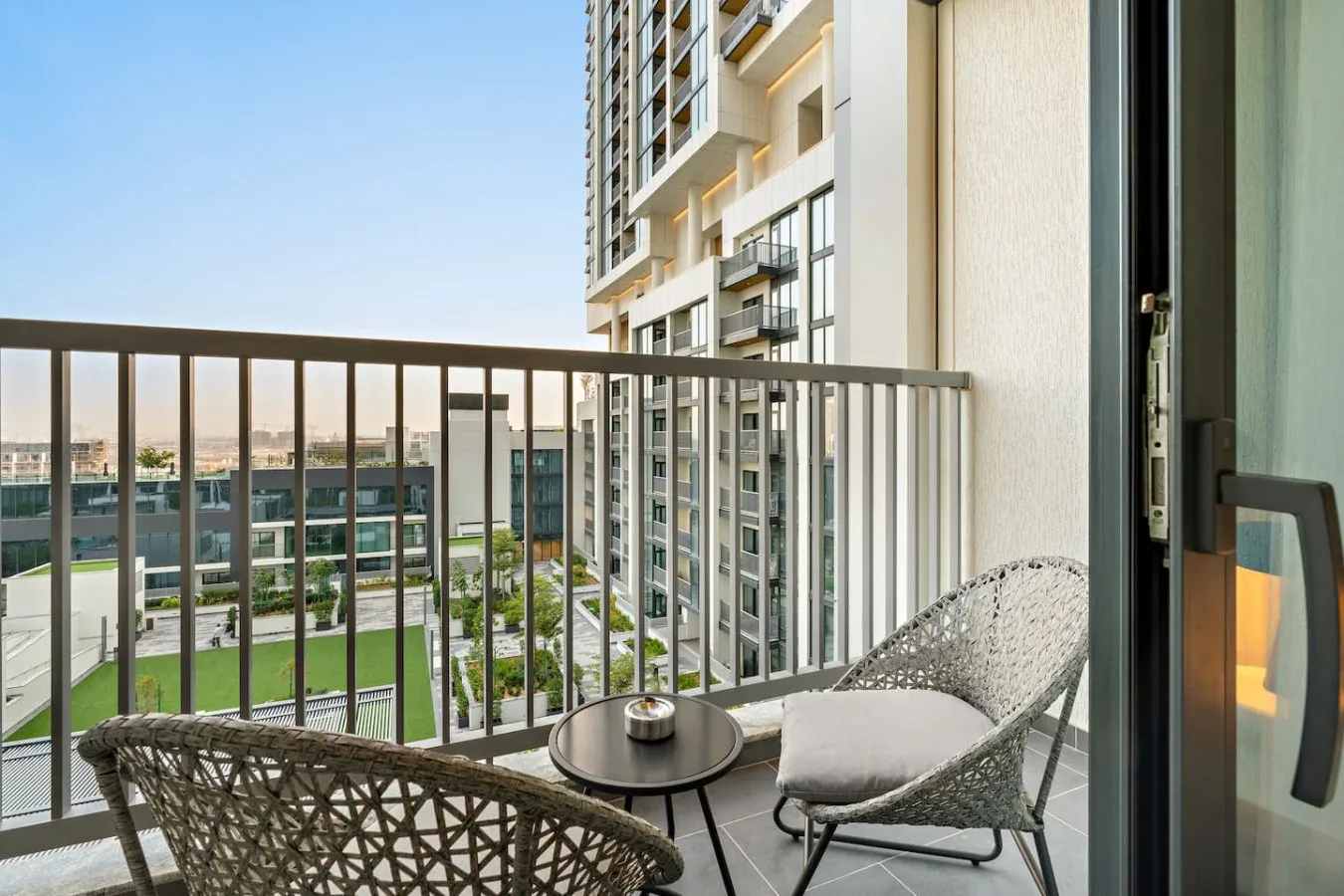 A balcony with outdoor seating overlooks nearby buildings and landscaped grounds.