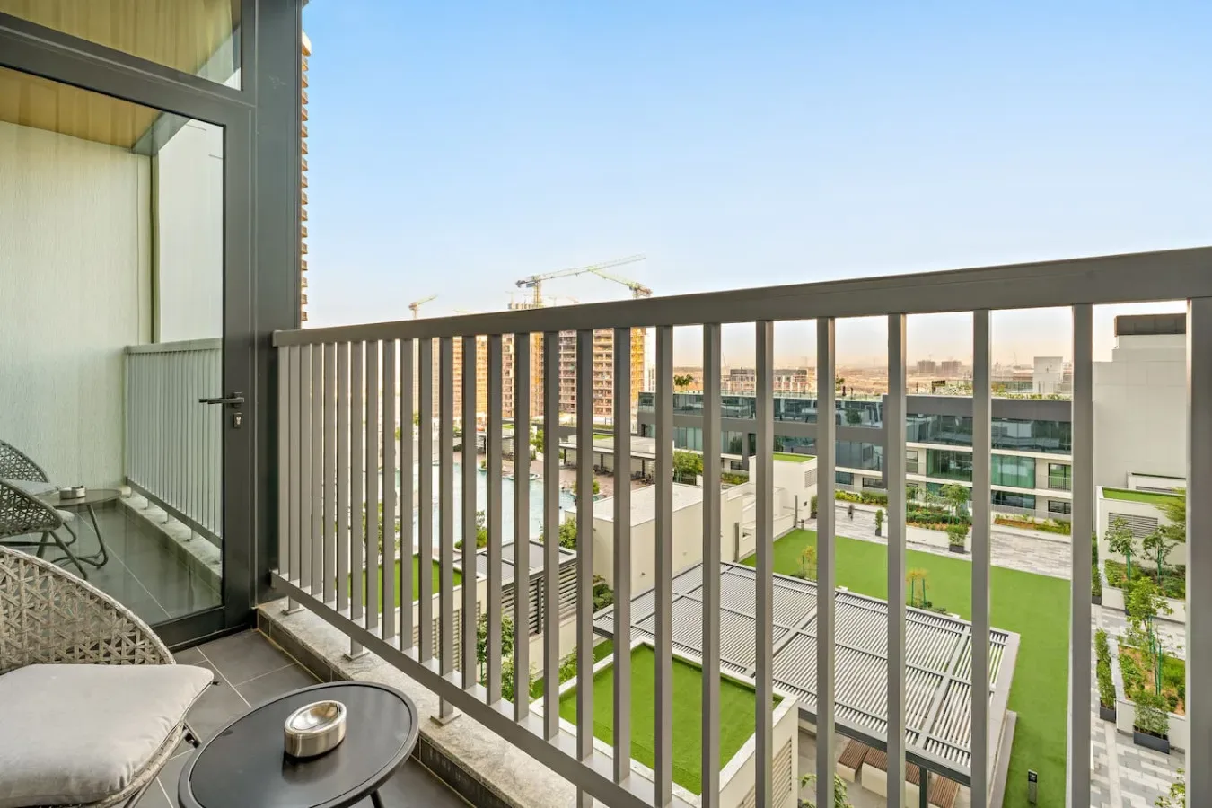 A balcony with outdoor seating overlooks nearby buildings and landscaped grounds.