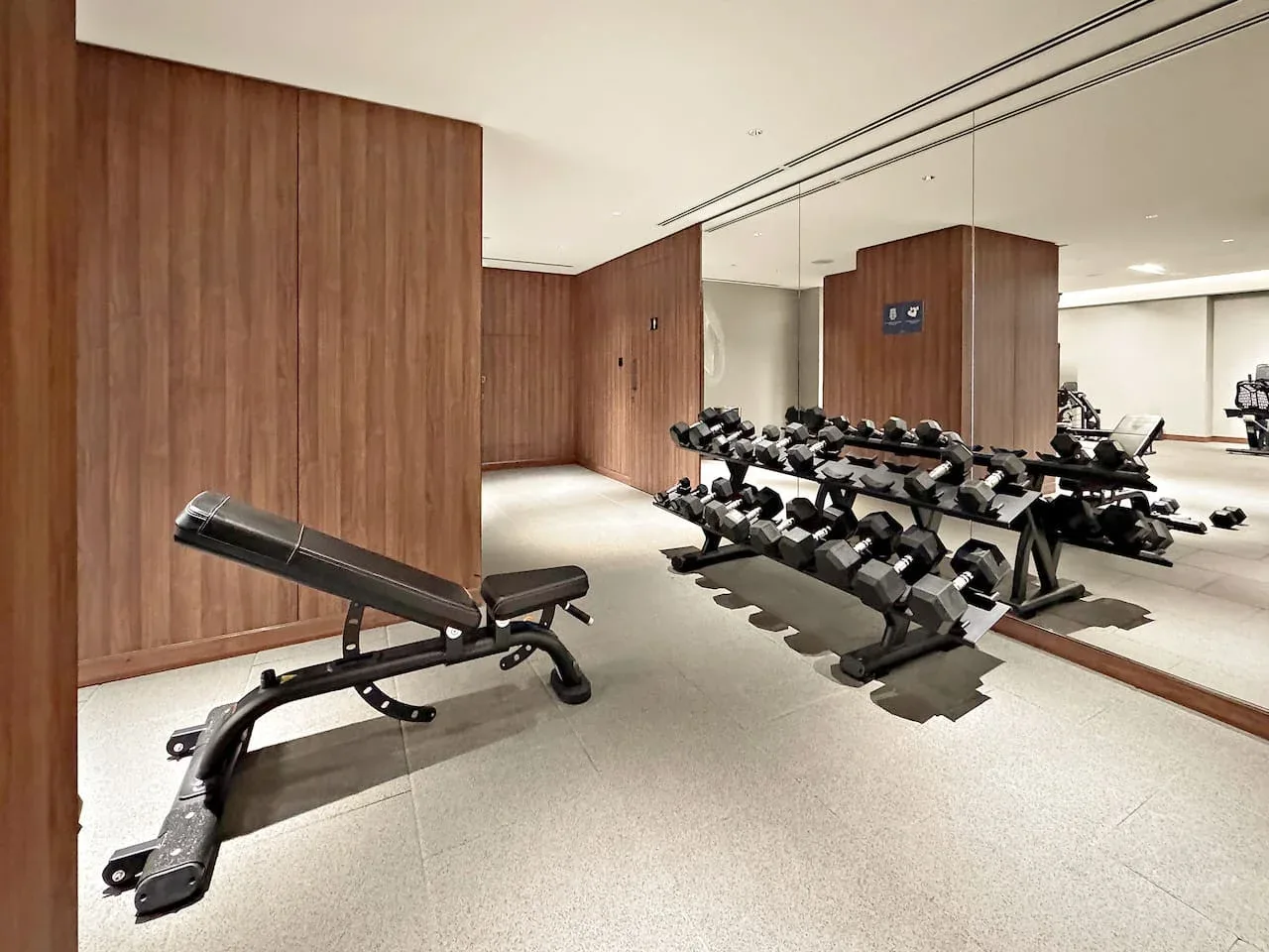 A gym with weight racks and an adjustable workout bench in front of mirrored walls.