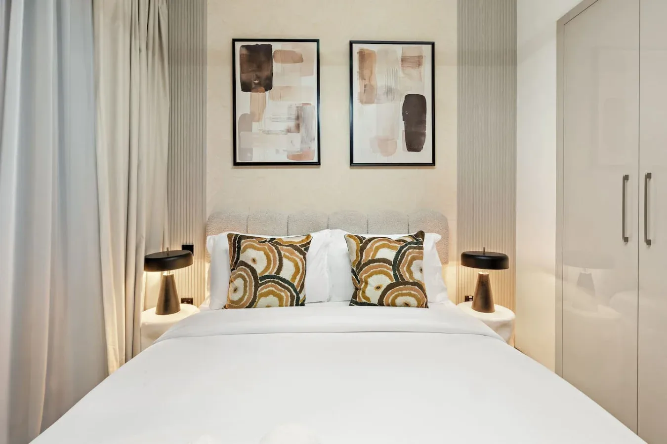 A bedroom with a neatly made bed, patterned pillows, and framed artwork.