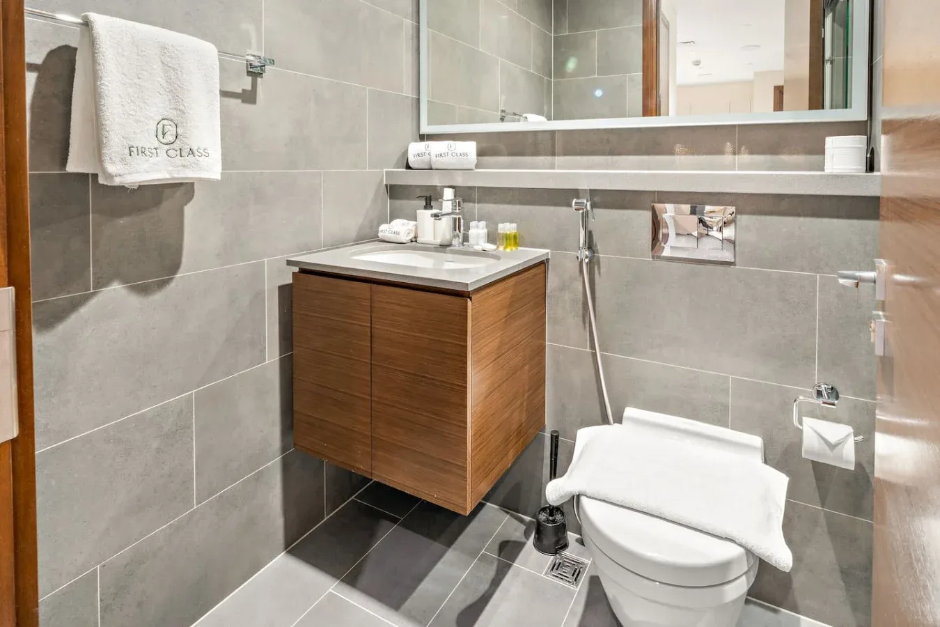 A tiled bathroom with a wooden vanity, mirror, and toilet.