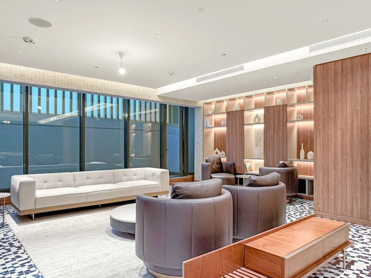A modern lounge features low seating, a long sofa, and illuminated display shelves.