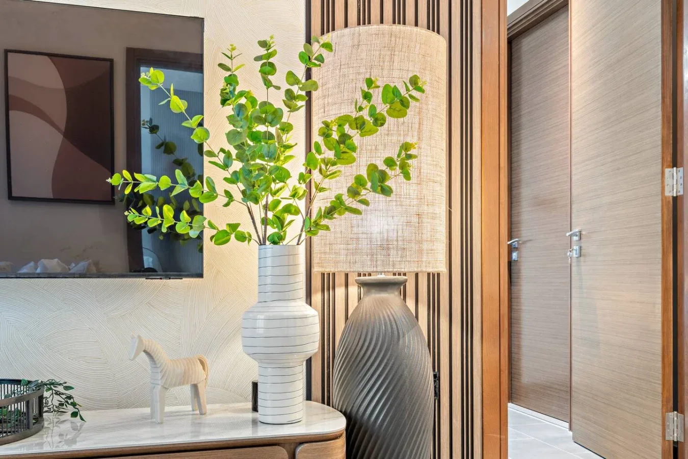 A modern interior corner features decorative vases and leafy branches beside a wall-mounted screen.