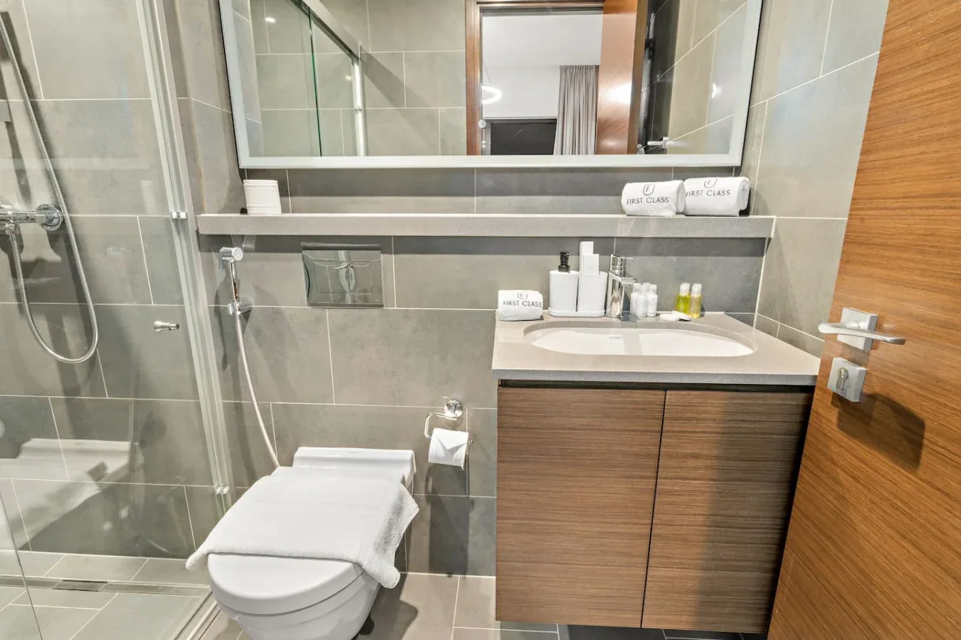 A tiled bathroom with a shower, toilet, and sink beneath a wide mirror.