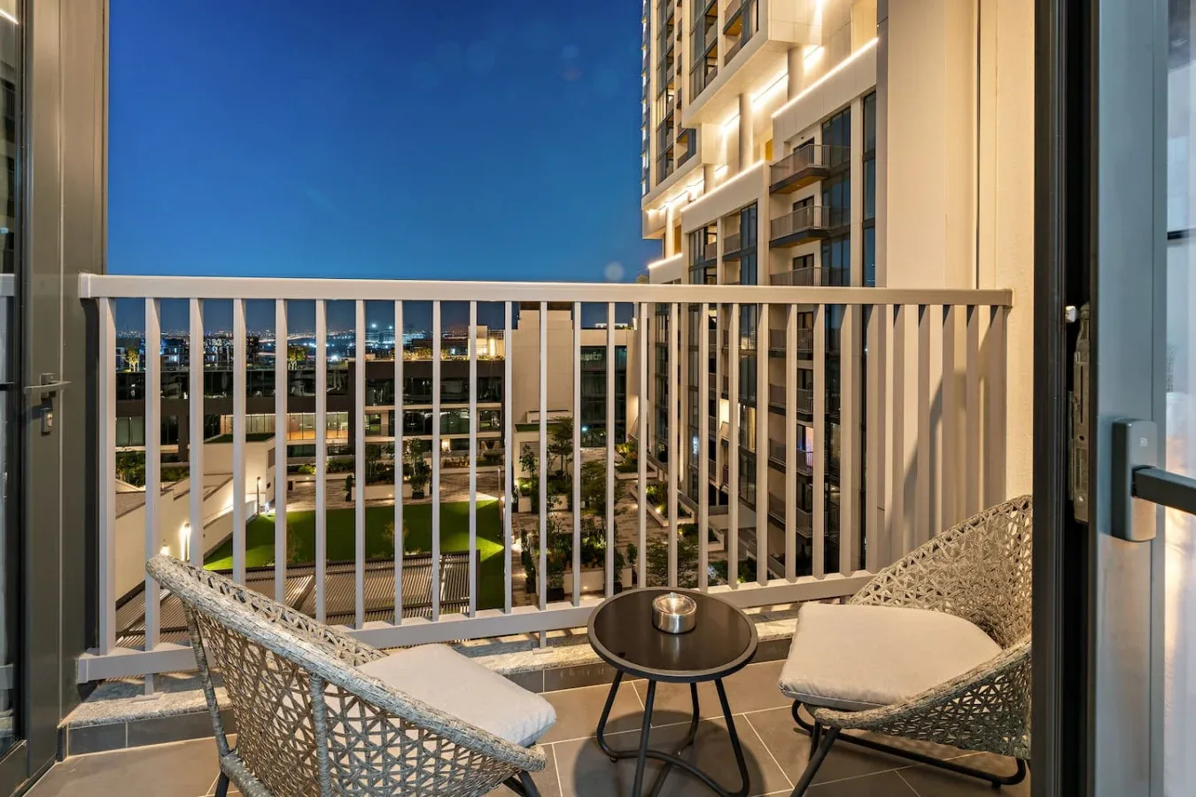 A balcony seating area overlooks illuminated buildings beneath the evening sky.