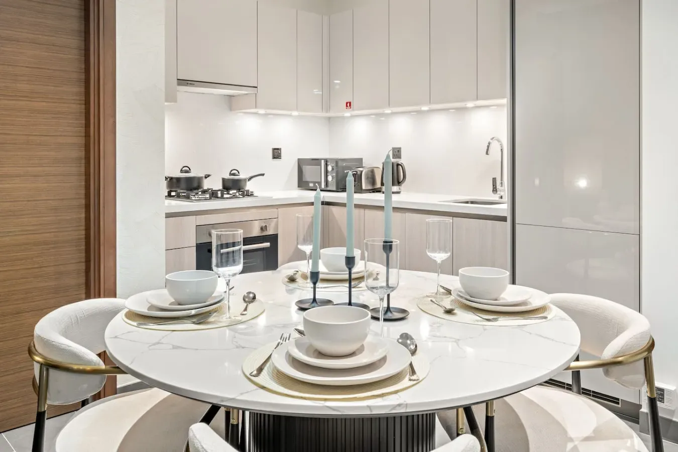 A dining table is set in front of a bright modern kitchen.