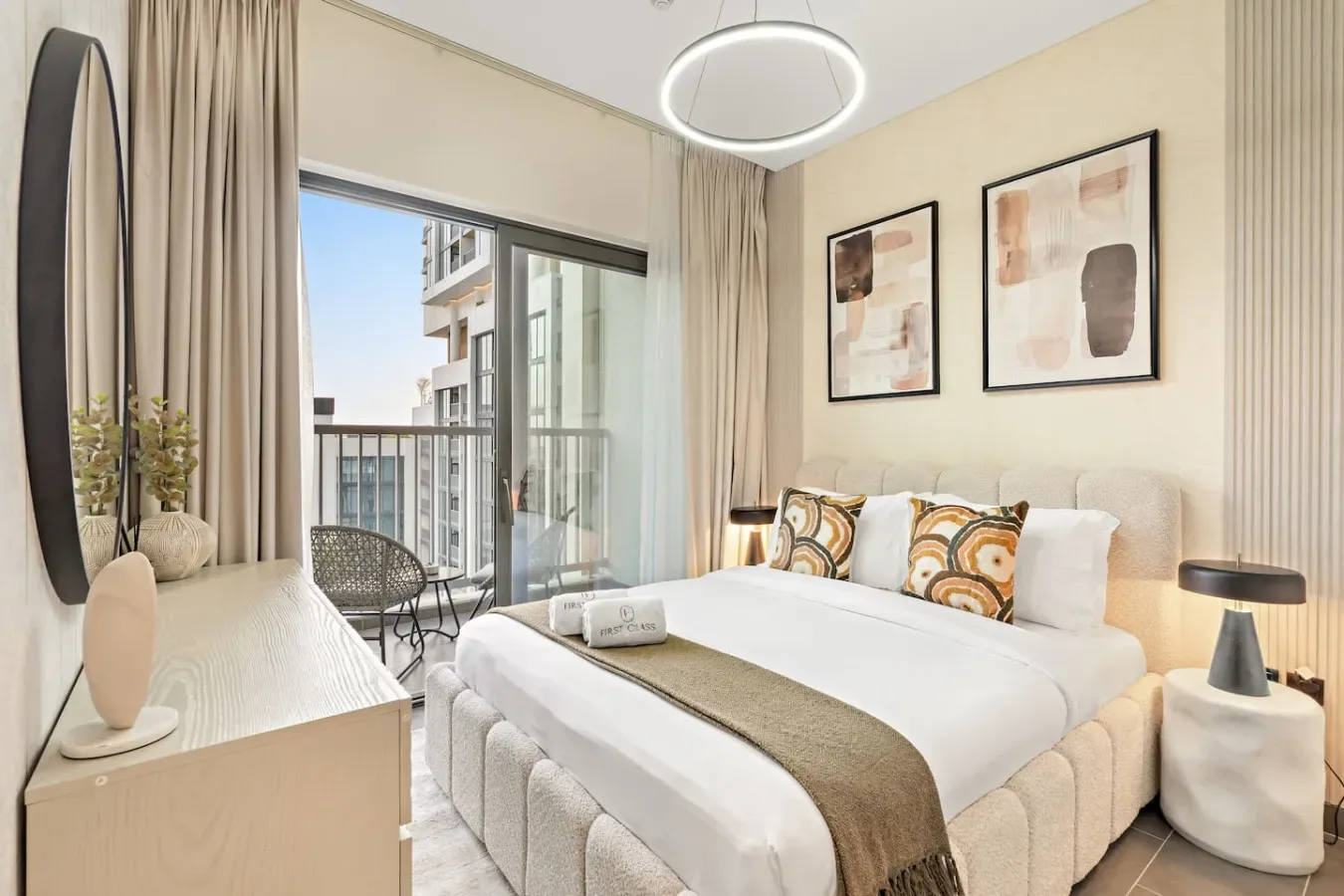 A bright bedroom with a neatly made bed, framed artwork, and a balcony door.