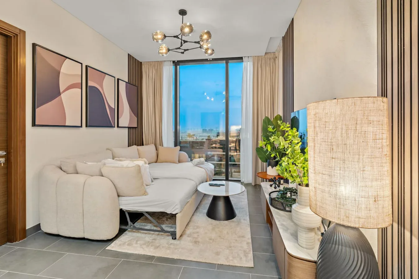 A living room with light-colored seating, framed artwork, and a large window.
