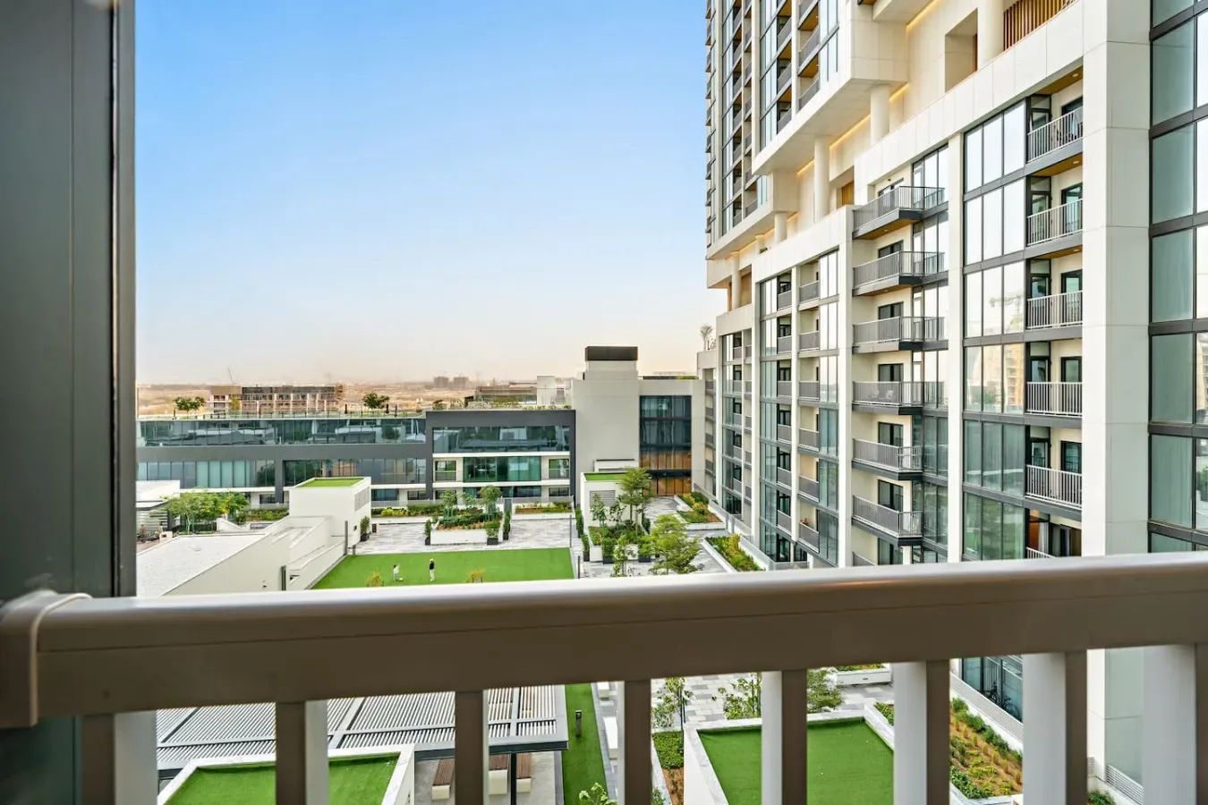 A balcony overlooks landscaped grounds and modern apartment buildings.