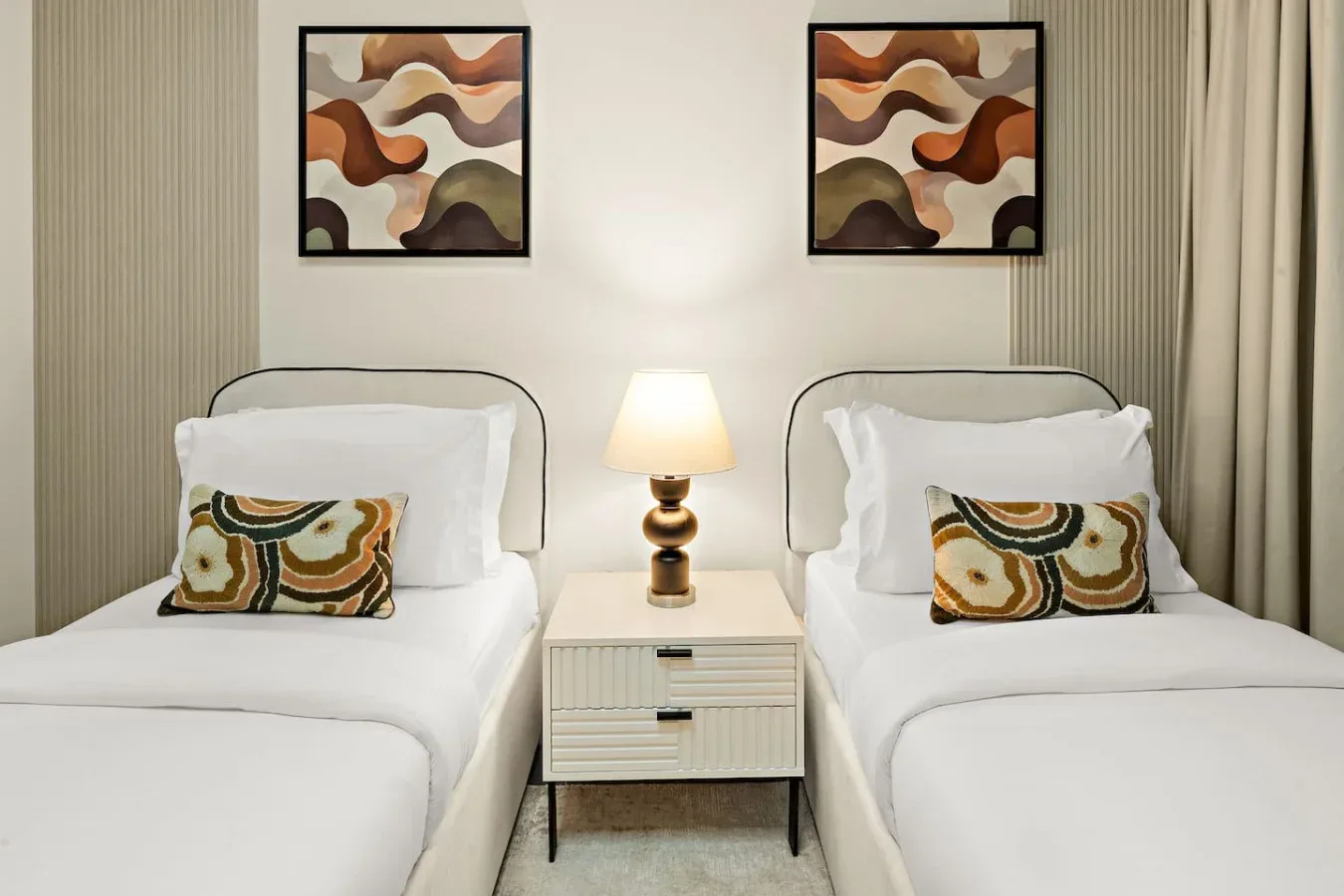 A bedroom with two beds, a bedside table, and matching abstract artwork.