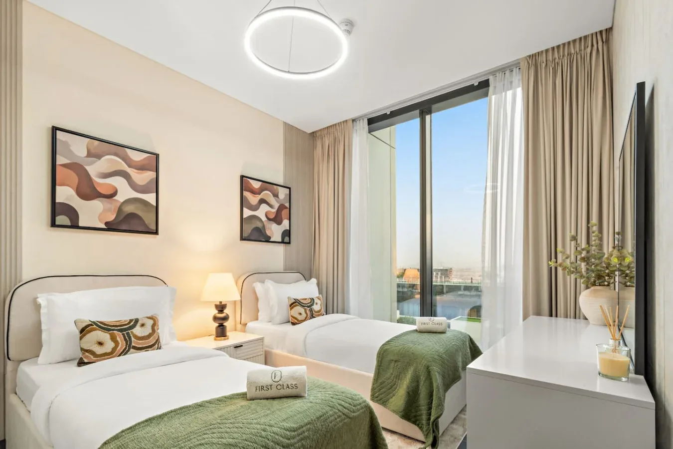 A bright bedroom with two beds, framed artwork, and a large window.