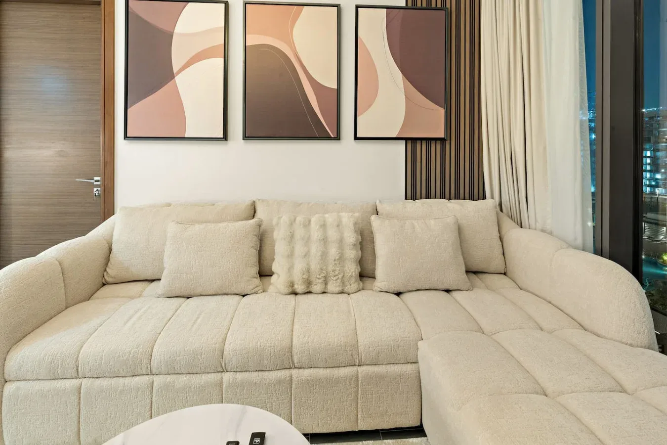 A bright living room with a cream sectional sofa and abstract wall art.
