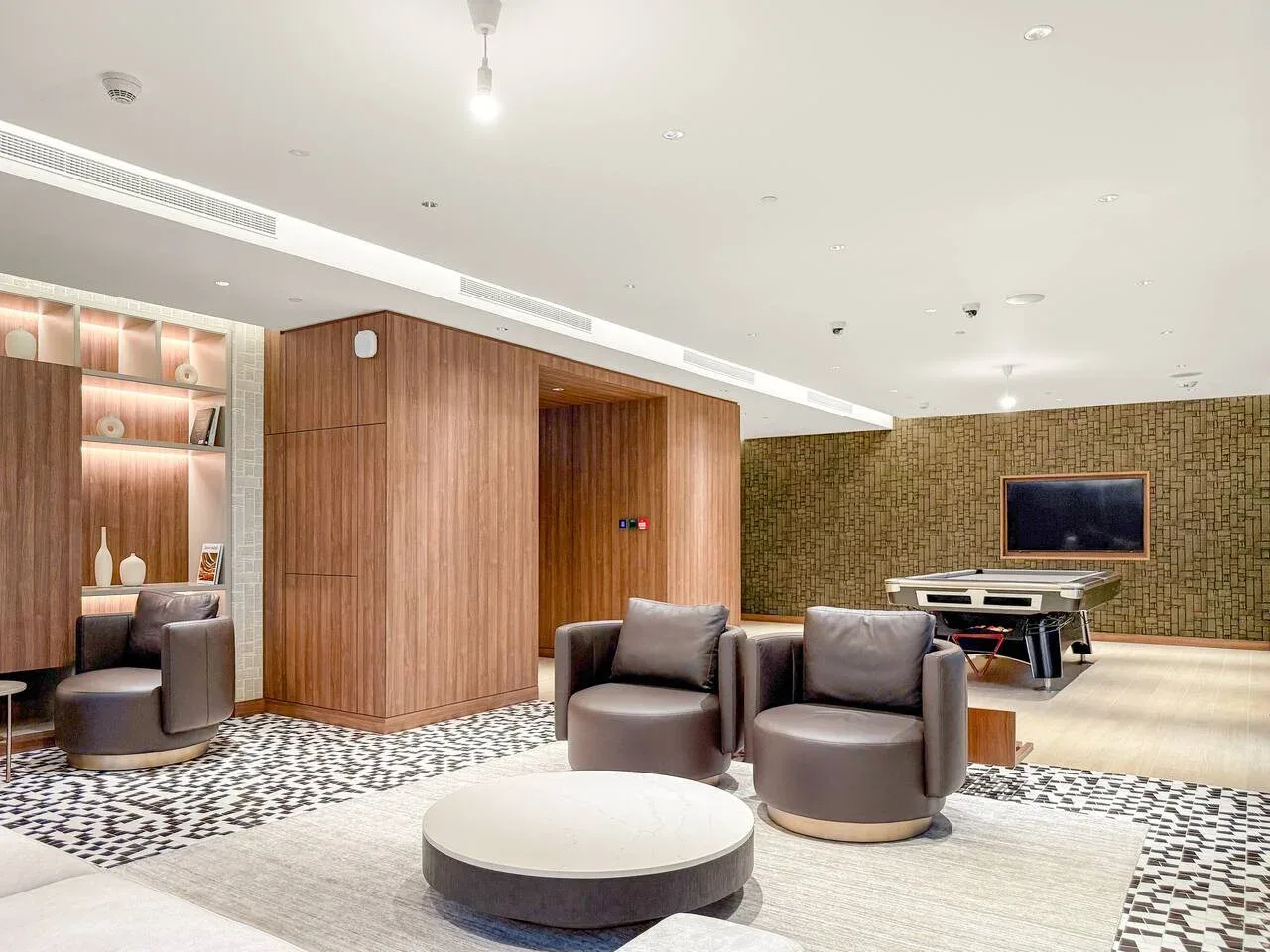 A modern lounge with upholstered seating, a round table, and a patterned carpet.