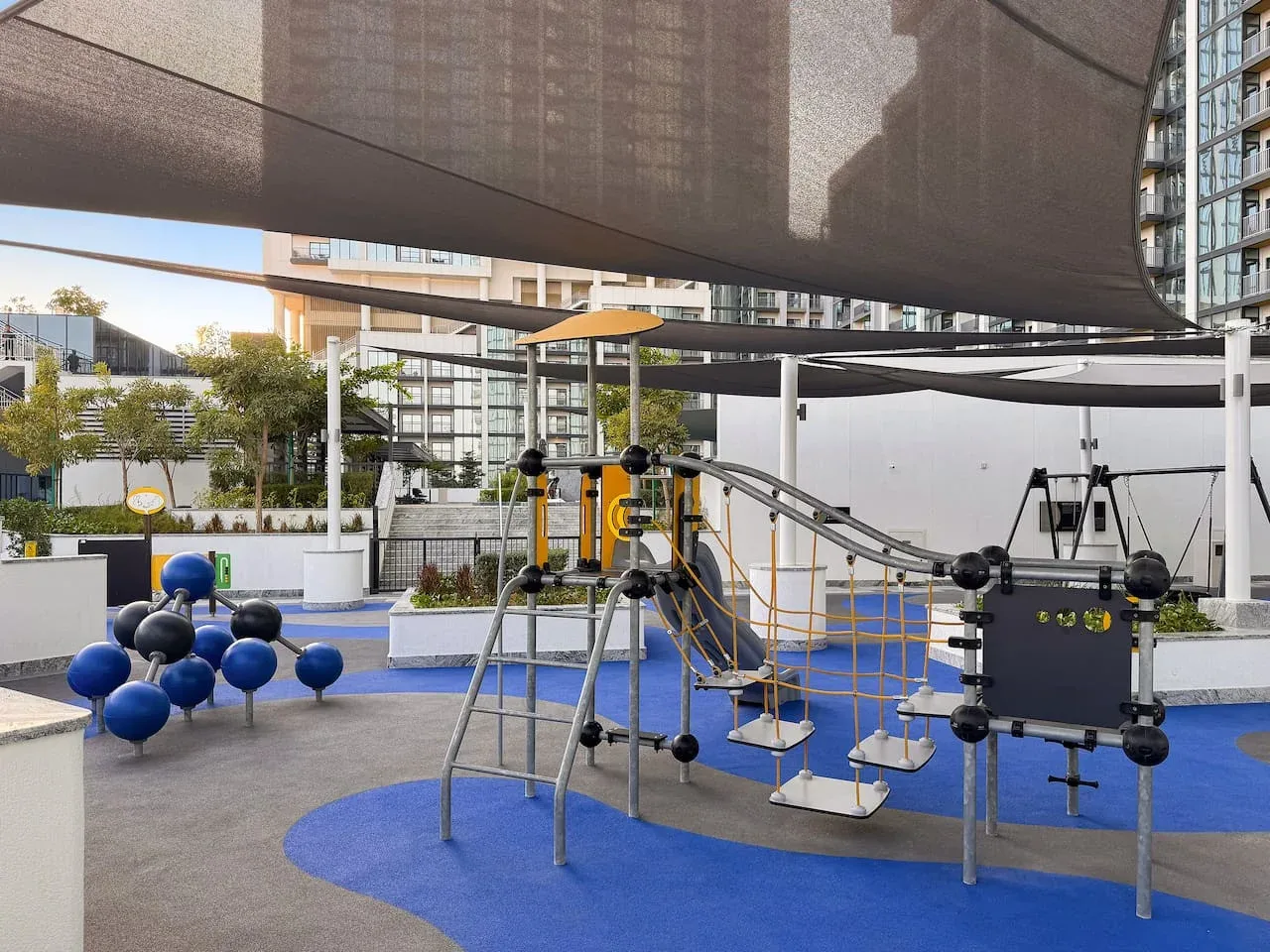 An outdoor fitness area features exercise equipment beneath a large shade canopy.