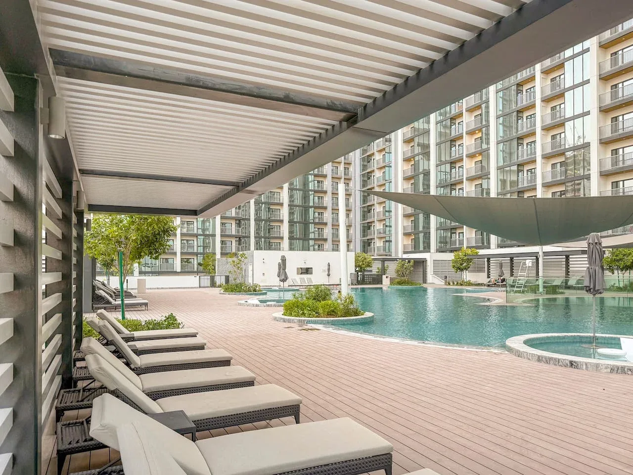 An outdoor pool and surrounding lounge seating sit beside a modern residential building.