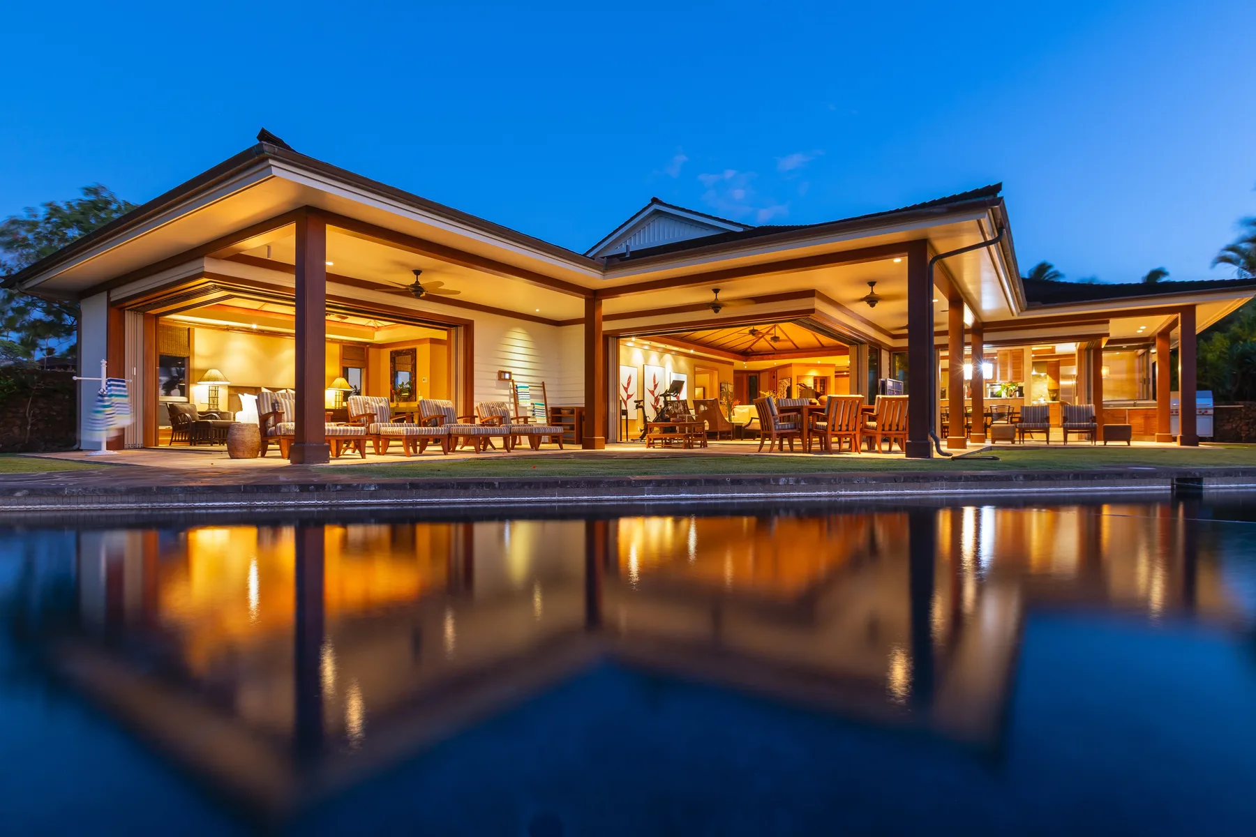 A modern house with warmly lit open living spaces beside a reflecting pool.