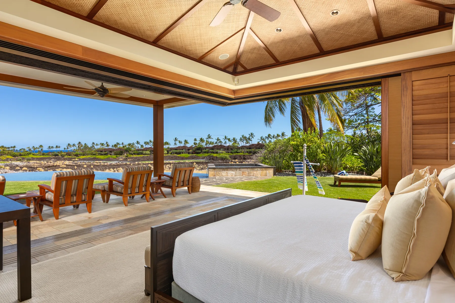 An open-air bedroom overlooks a patio with dining seating and a pool.