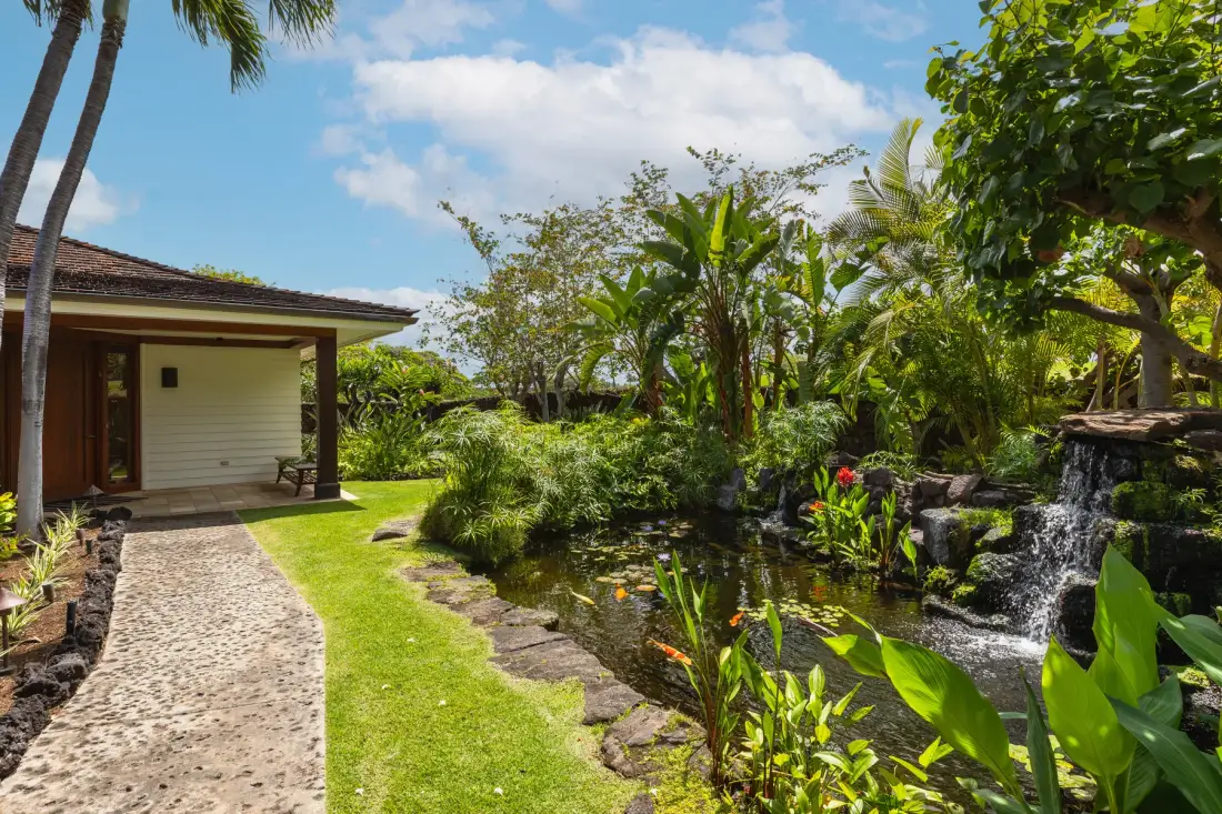 A tropical garden path curves beside a pond and small waterfall.