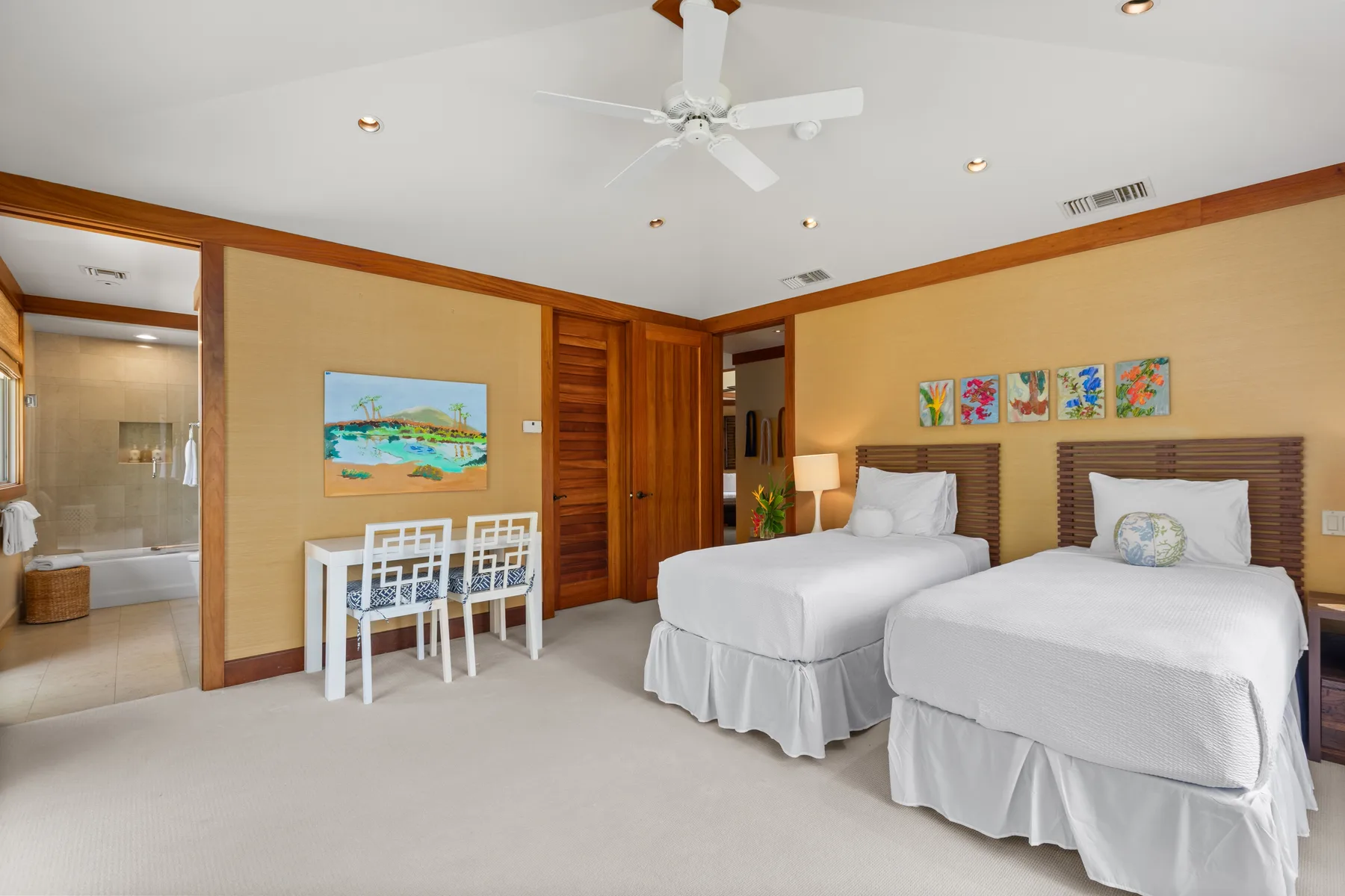 A bedroom with two beds, a small dining table, and an open bathroom doorway.
