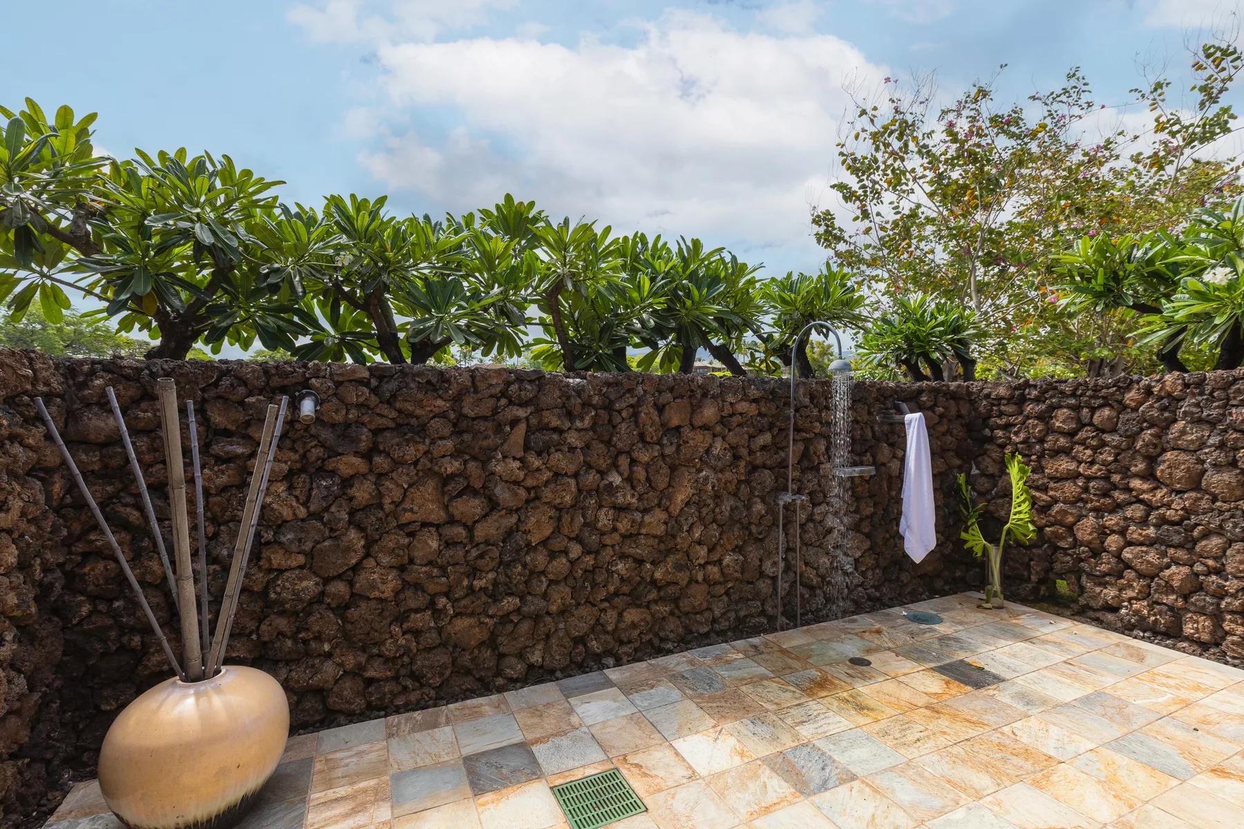 A paved outdoor patio beside a stone wall, with leafy trees overhead.