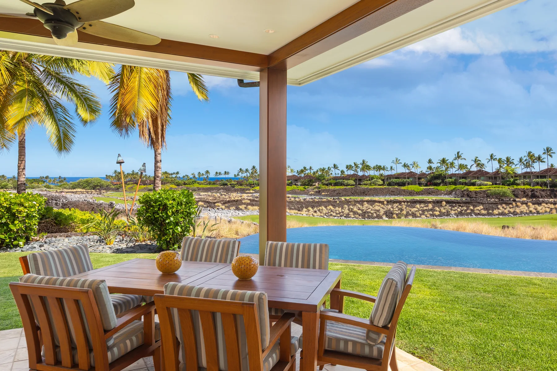 A covered outdoor dining area overlooks a grassy lawn and blue water.