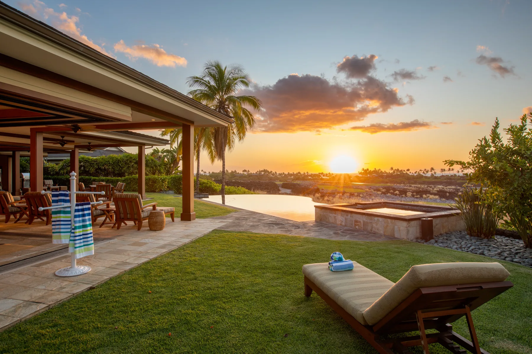 A patio and poolside lawn overlook the water at sunset.