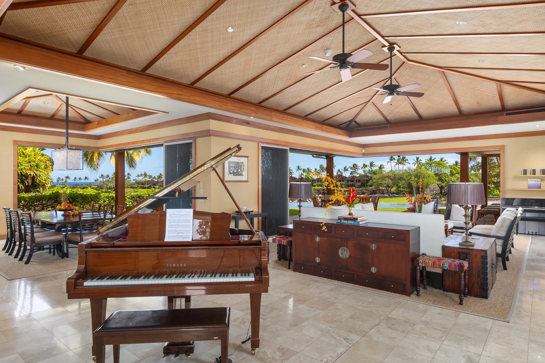 Una sala y comedor abiertos cuentan con un piano y vistas a la vegetación tropical.