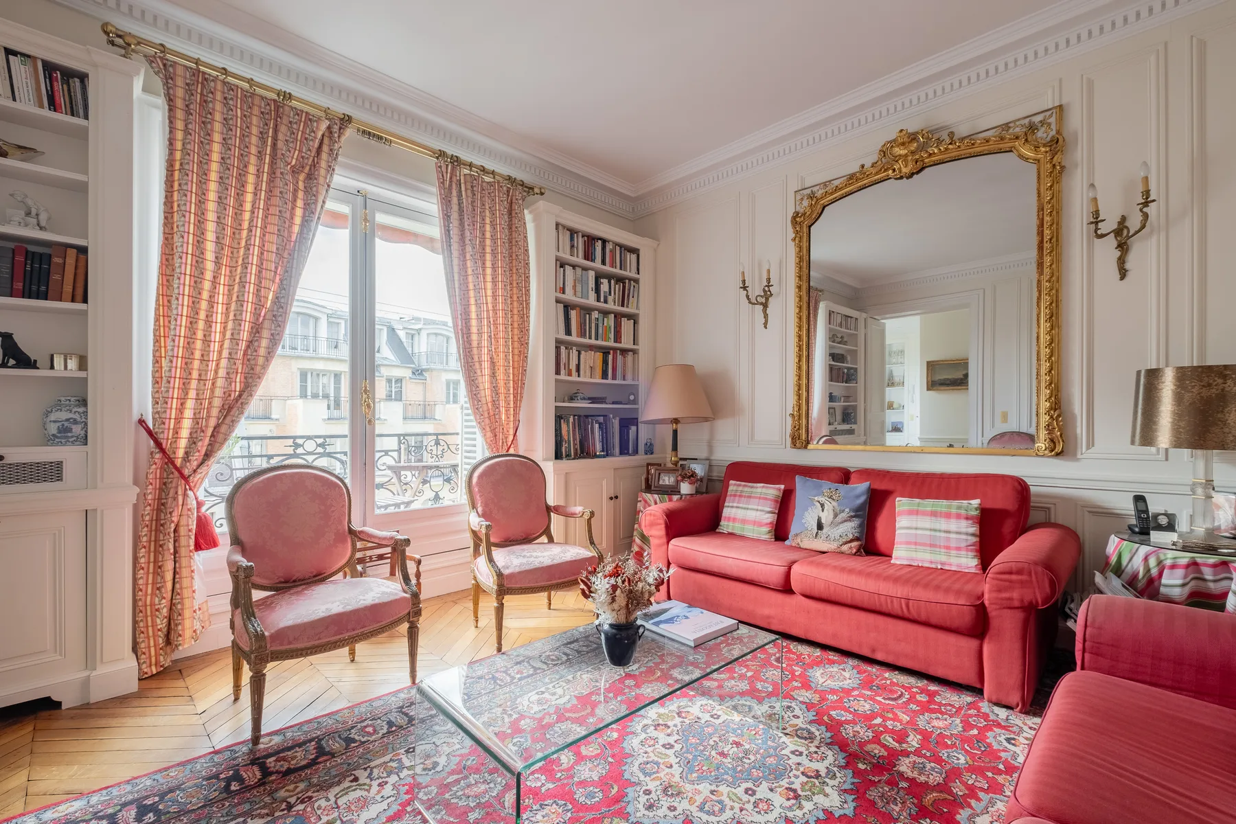 Una sala luminosa cuenta con asientos rojos, ventanas altas y alfombras estampadas.